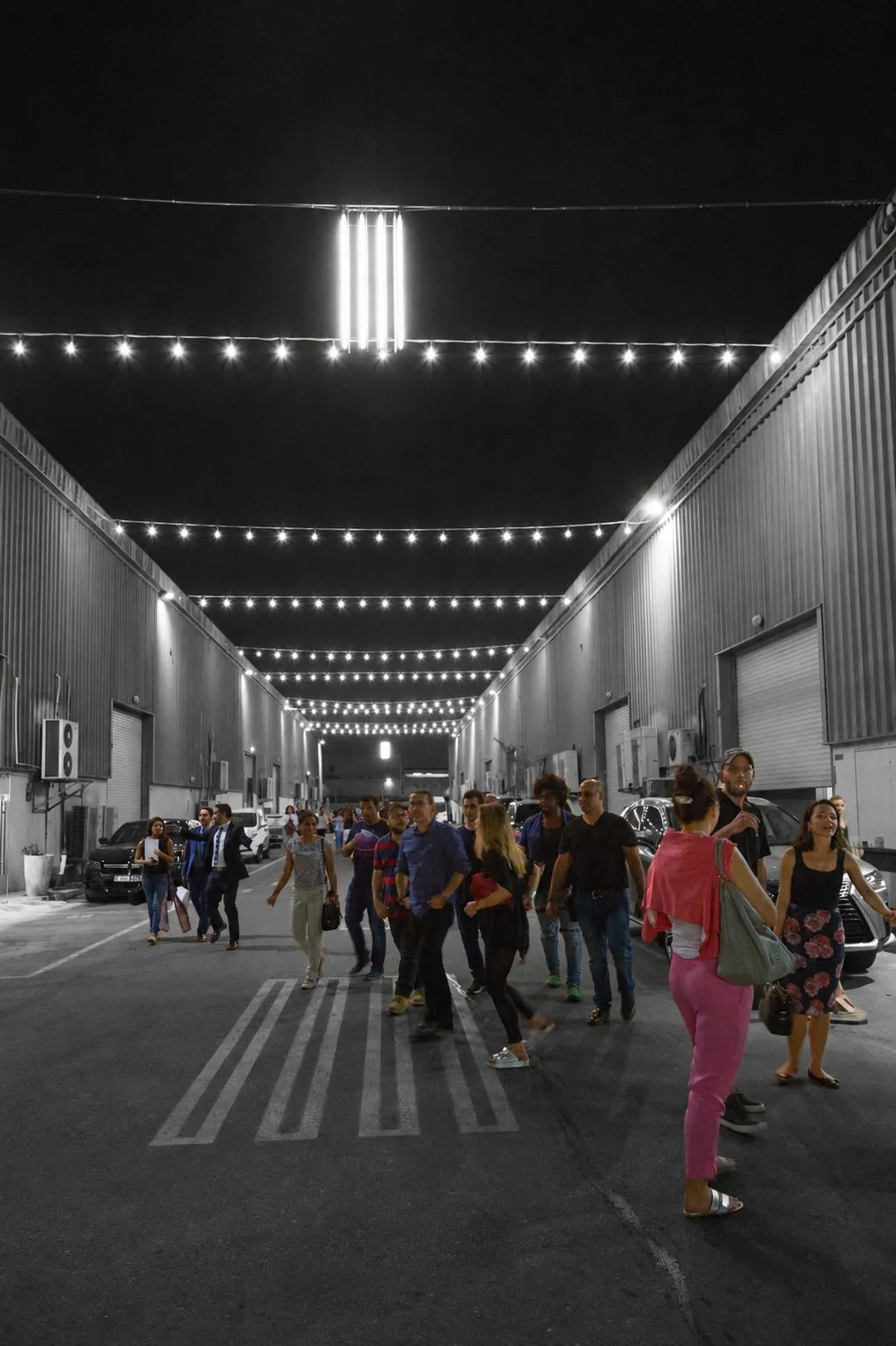 Visitors walking under festoon lights between warehouses at Alserkal Avenue at night
