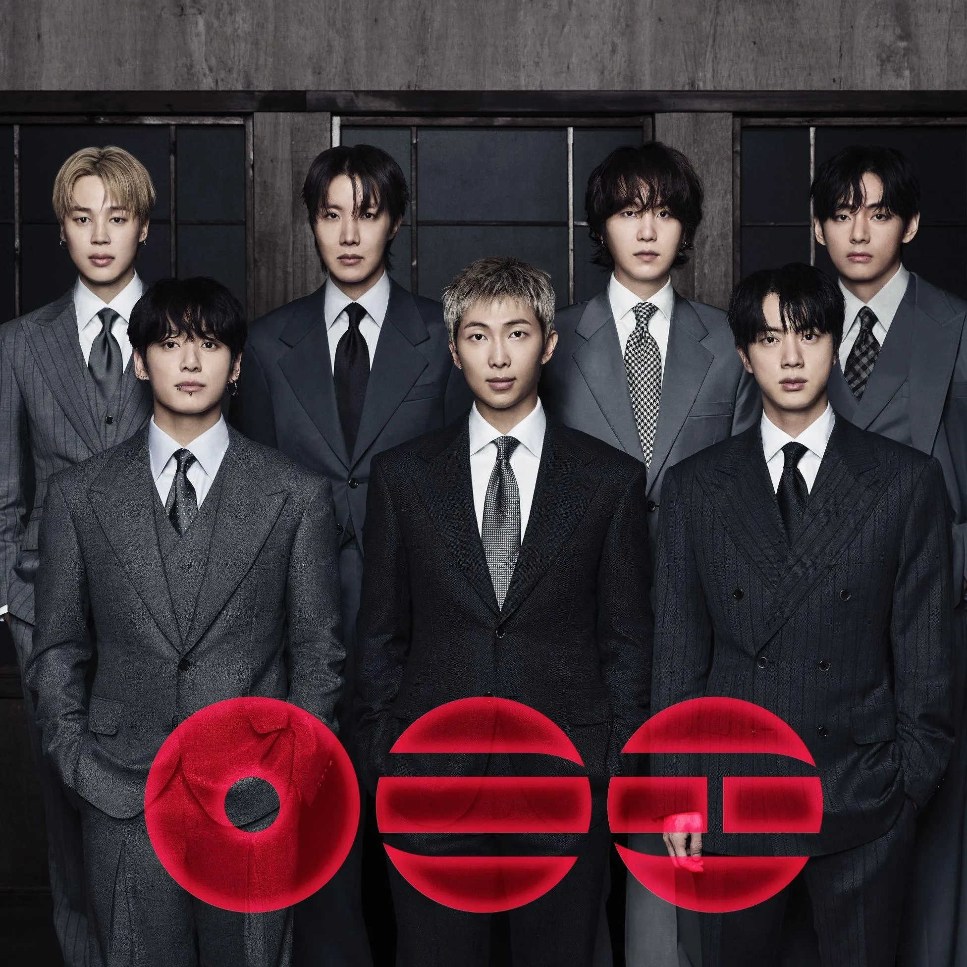 Seven BTS members in dark suits, with three red disc graphics across the lower part of the group portrait