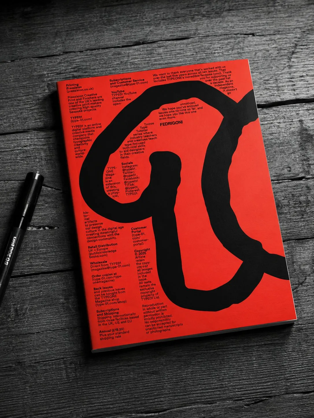 A red TYPE01 magazine with oversized black lettering on a monochrome wooden desk