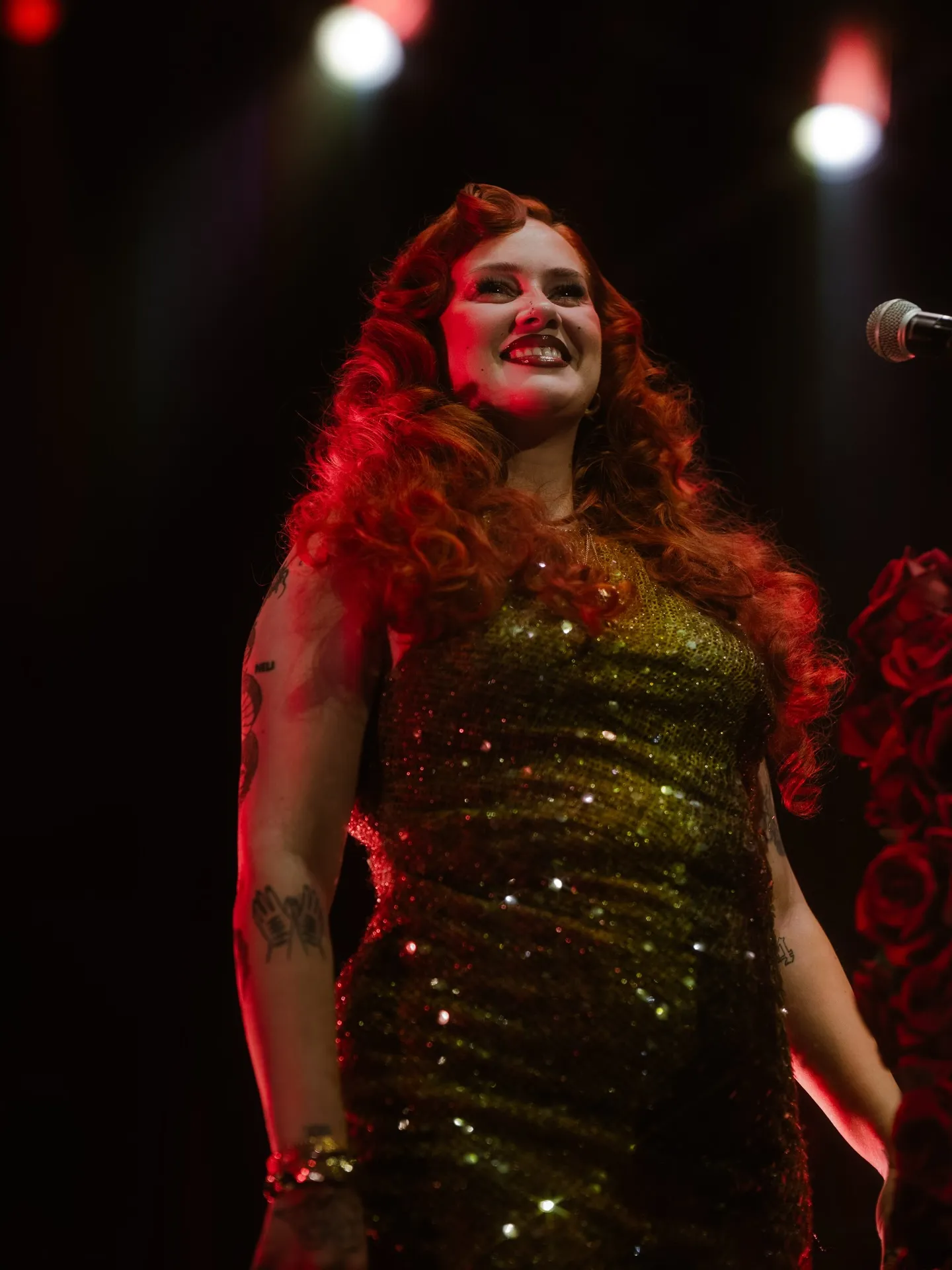 A singer with long red hair performing under red stage lights at Limitless Live