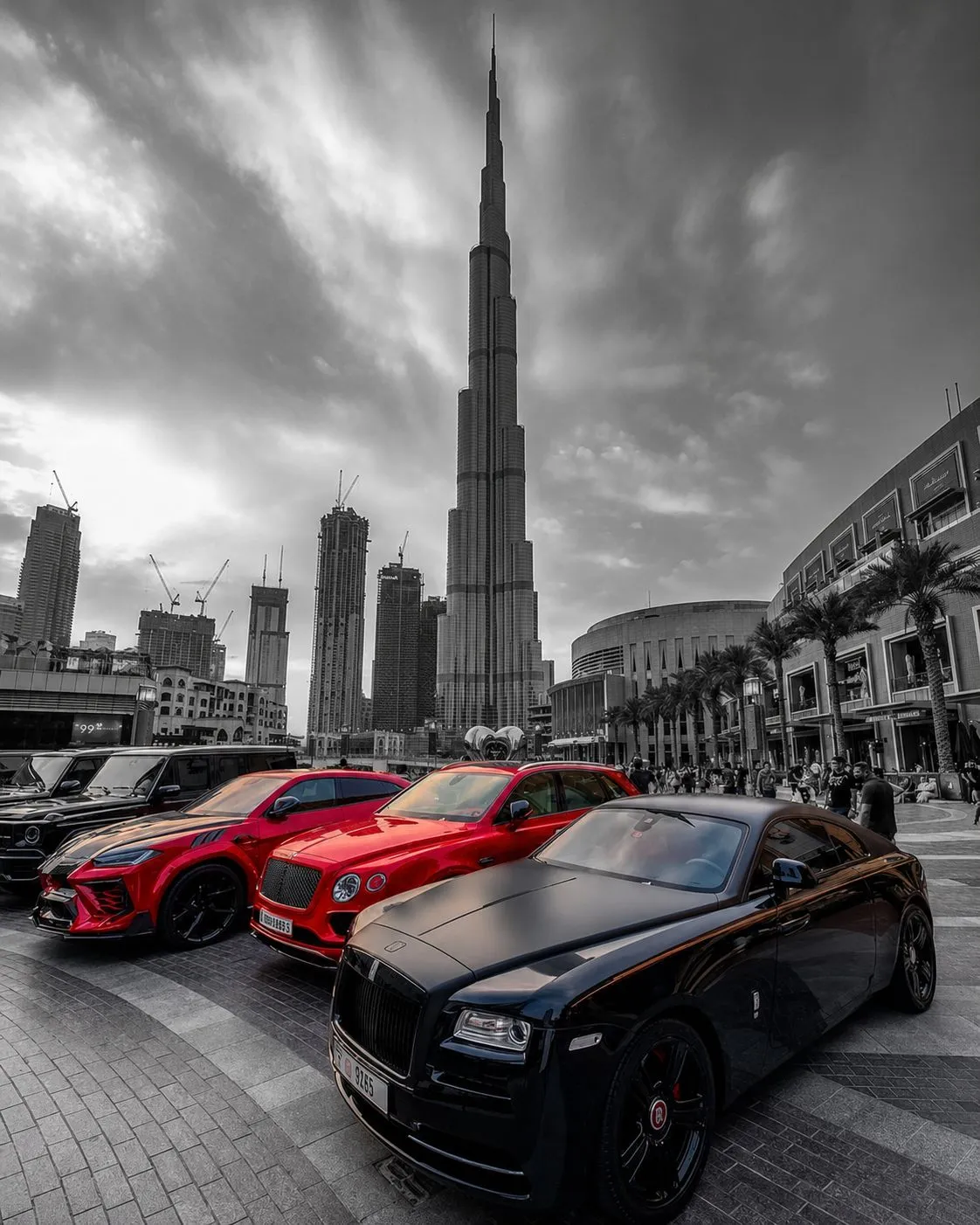 Supercars parked beneath the Burj Khalifa, two red cars the only colour in a monochrome scene